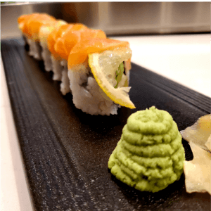 A salmon roll with lemon on a slate plate, served with wasabi and pickled ginger